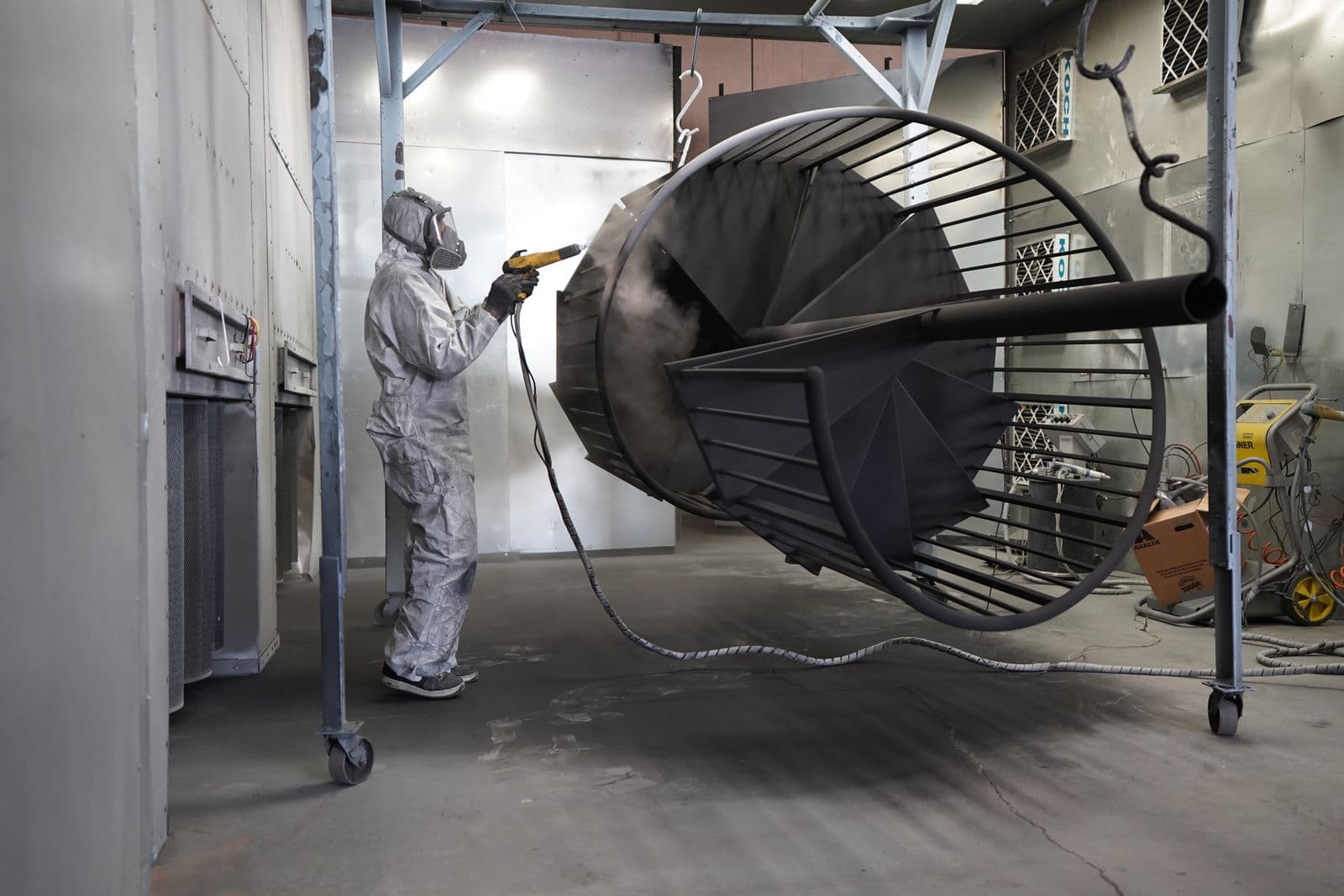 Pintor industrial aplicando pintura a pistola sobre una estructura metálica con equipo de protección en Bizkaia